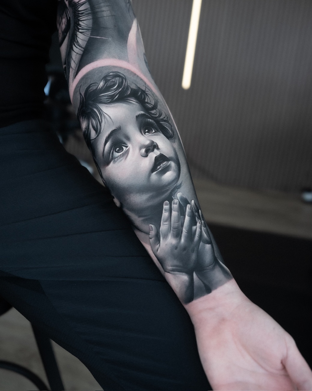 Realism tattoo of a child's face and hand on a forearm