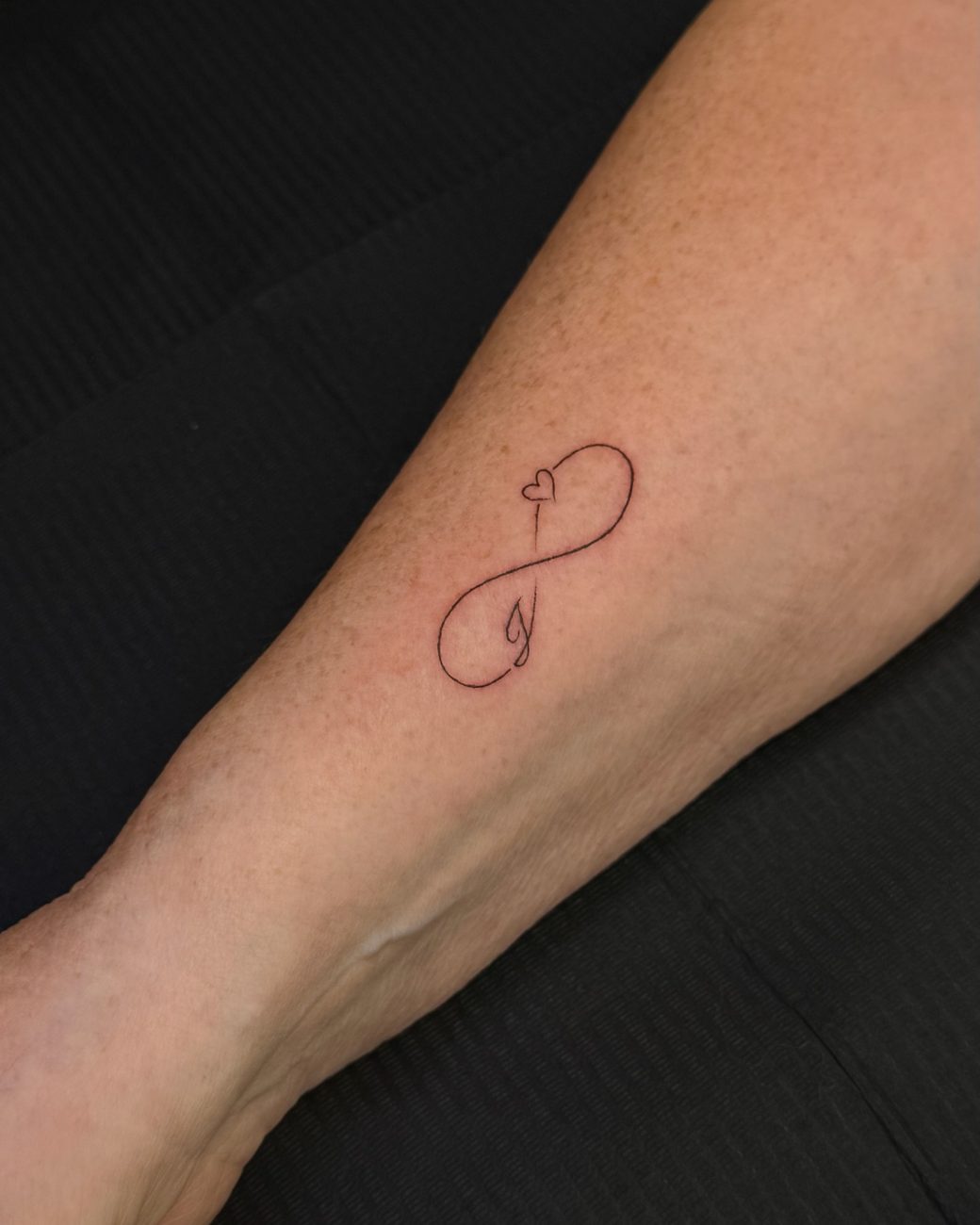 Fine line infinity and heart tattoo on a forearm