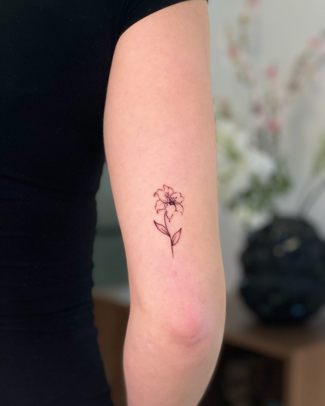 Fine line lily tattoo on an upper arm