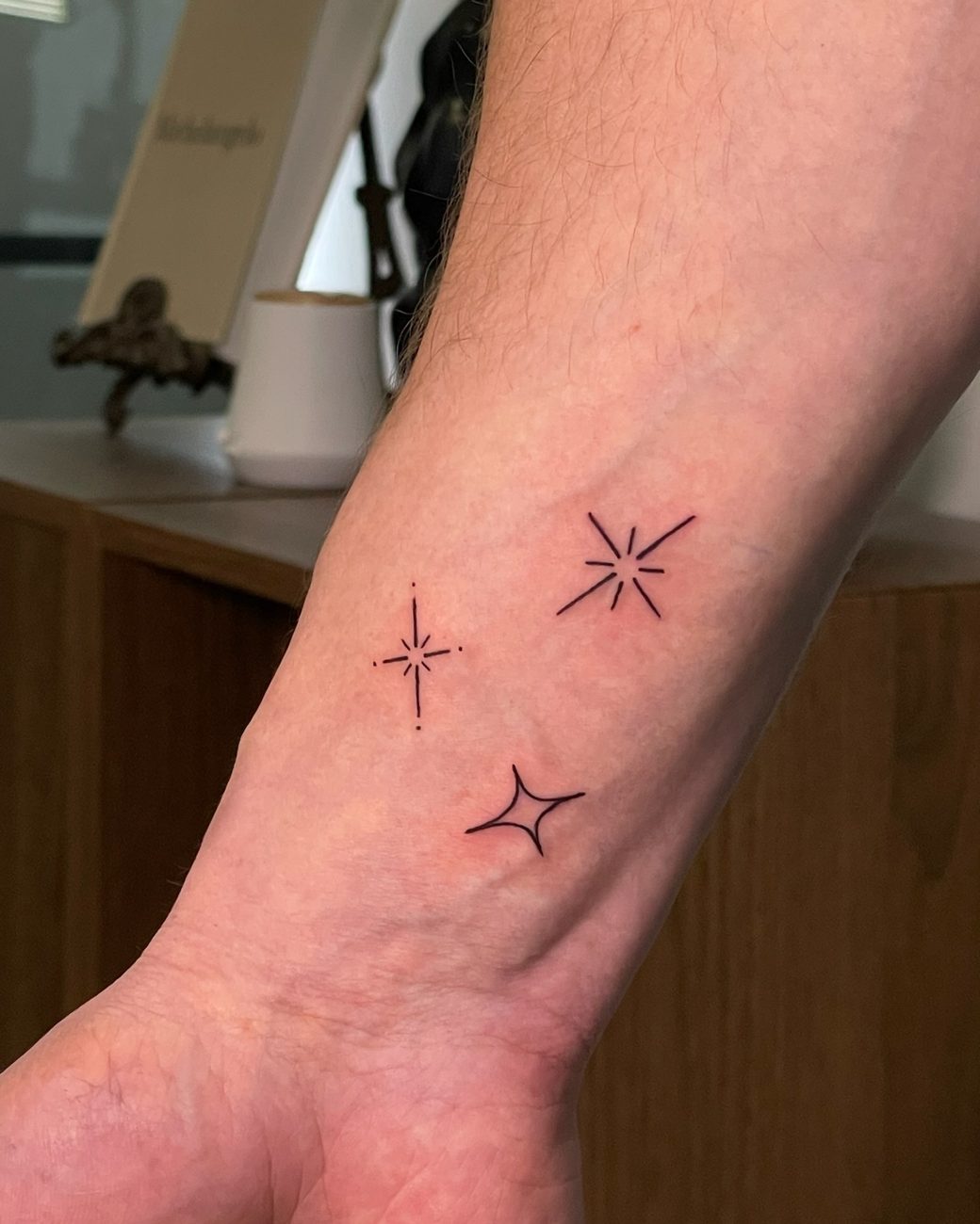 Fine line sparkle and star tattoos on a wrist